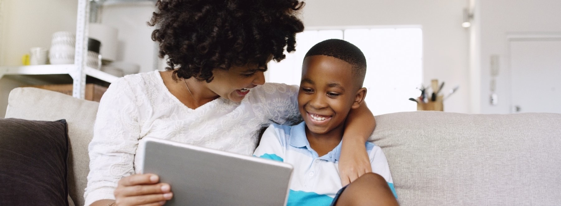 A smiling parent and child sit on the couch while looking at a survey on a tablet.