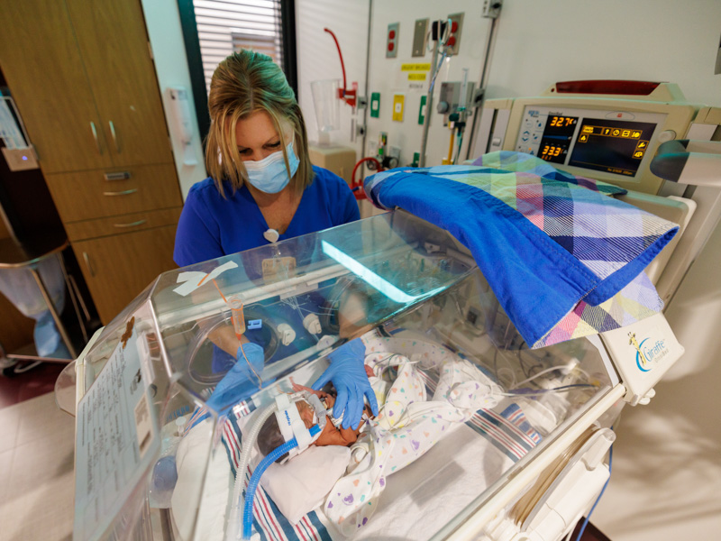 NICU occupational therapist Katherine McAuley reaches into an Isolette to reposition 2-week-old Ja'Dyn Washington, born three months early and weighing less than 3 pounds. Joe Ellis/ UMMC Communications