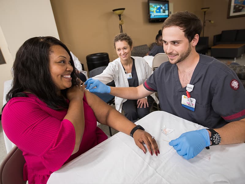 Briana Thompson, UMMC accreditation specialist, receives her annual flu shot from Seth Batton, a Hinds Community College nursing student, while fellow Hinds nursing student Collins Davis looks on Oct. 23 in the Verner Holmes Learning Resource Center.