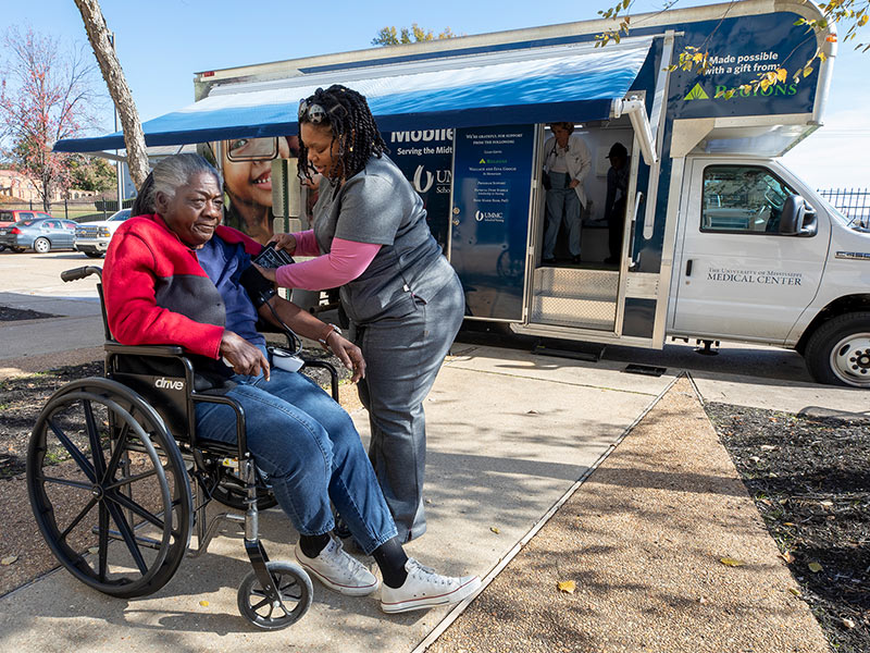 Betty Moore, Jackson Manor resident, gets her blood pressure checked by Micha'el Sheriff, patient care technician, in front of the UNACARE mobile clinic.
