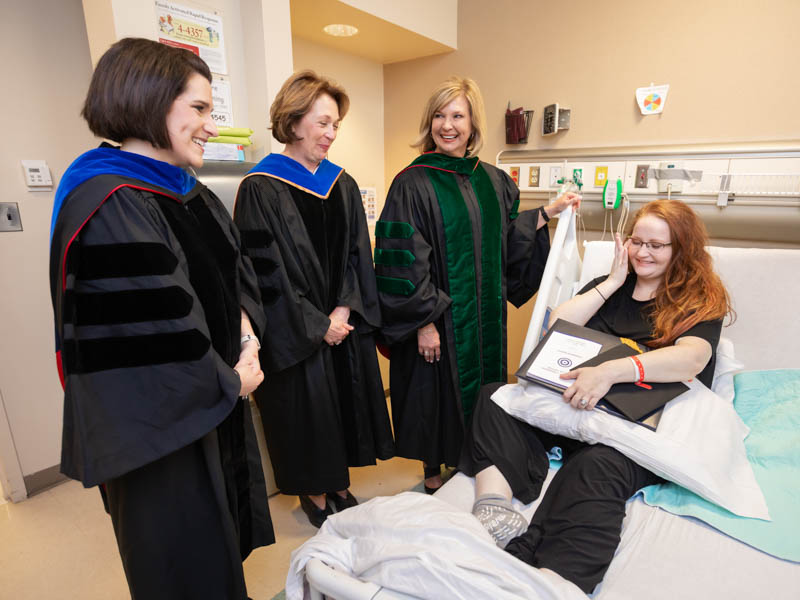 Sarah Herrington is overwhelmed by the kindness of those who brought graduation to her hospital room. With her are Dr. Kristi Moore, left, Dr. Jessica Bailey and Dr. LouAnn Woodward.