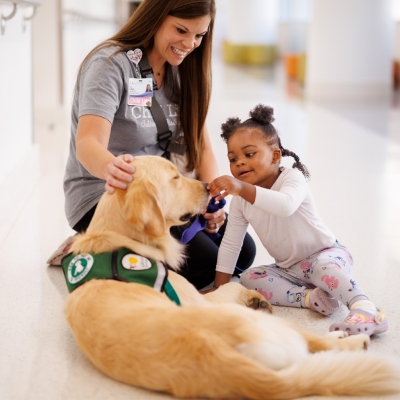 Child pets dog while nurse supervises.