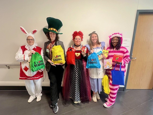 Group portrait of five Child Life staff members wearing ALice in Wonderland costumes and holding toy goody bags.