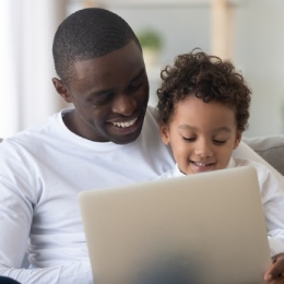 Man holding child in lap while looking at laptop.