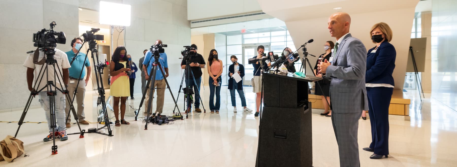 In the lobby of the School of Medicine, Dr. Alan Jones addresses a pool of reporters and accompanying videographers as Dr. LouAnn Woodward looks on.