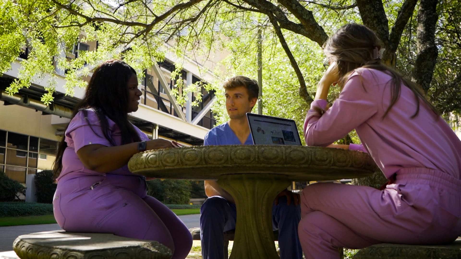 Three students conversing at a picnic table outdoors