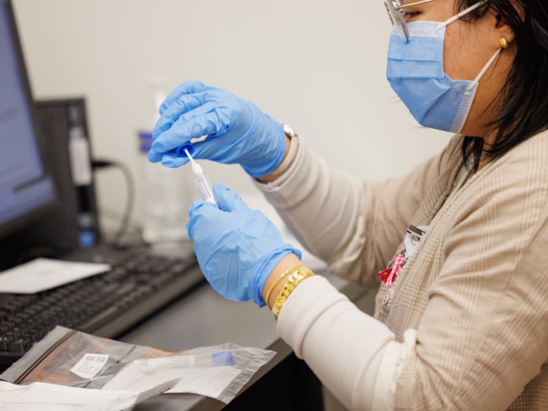 A genetic counselor places a cotton-tipped swab into a test tube.