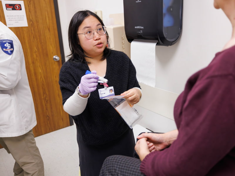 A gloved genetic counselor holding a genetic sample talks with a patient.