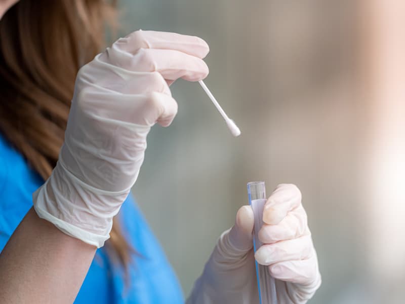 Gloved hands are shown with the person holding a cotton-tipped swab and a test tube.