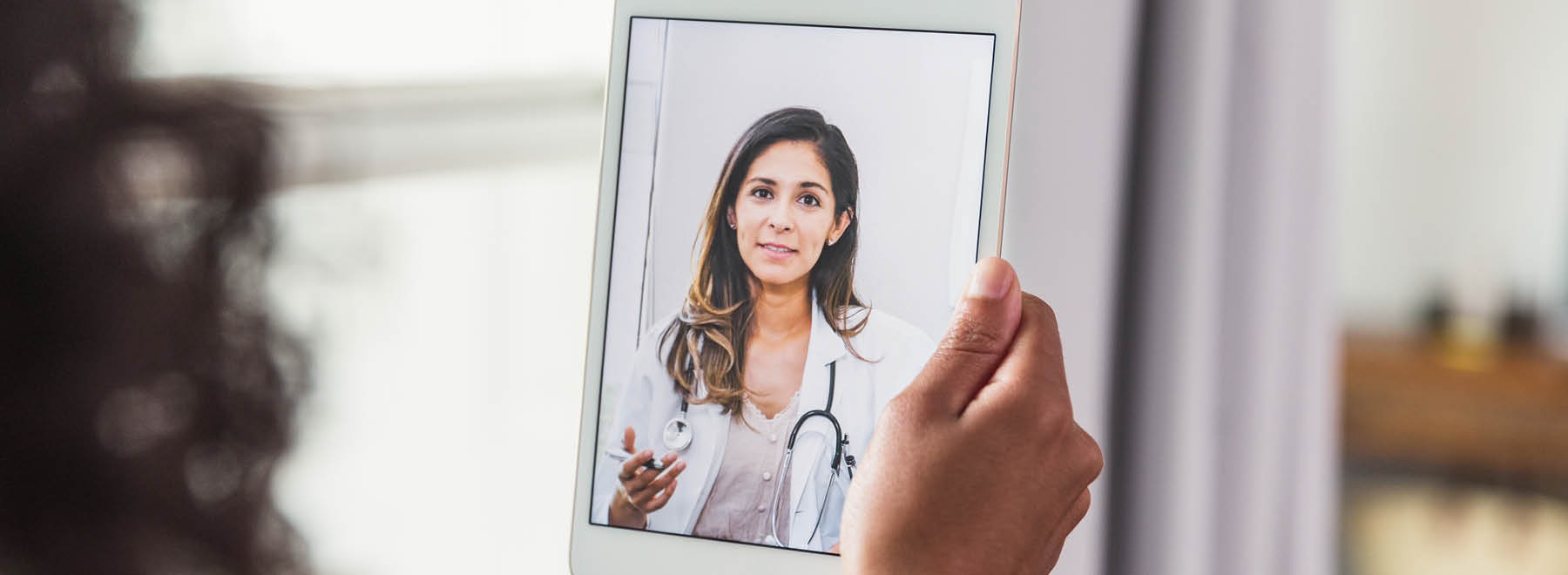 Patient holding tablet with telehealth provider on-screen.