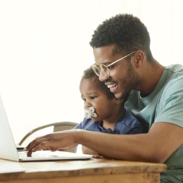Father holds child while making an online appointment.