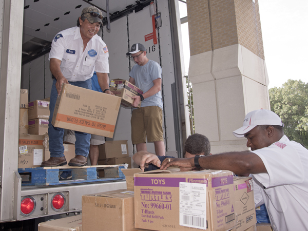 Walmart employee Rickey Oliver and volunteer Joseph Miller pass down boxes, unload truckloads of donated toys.