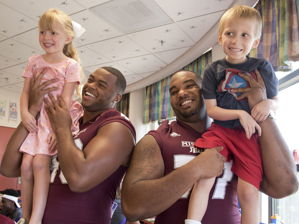 Campbell and his sister Avery are entertained by Mississippi State University football players Ryan Brown, left, and Rufus Warren during a team visit July 2015 to Batson Children's Hospital.