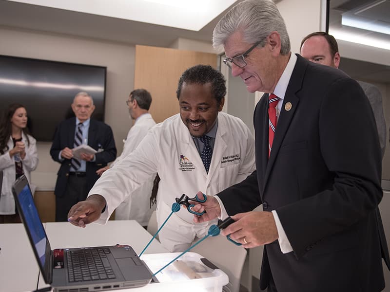 Dr. Michael Holder, left, associate professor of pediatric emergency medicine and executive director of simulation and interprofessional education, shows Gov. Phil Bryant how to play a game that simulates performance of surgery.