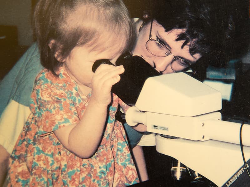 A young Paige Robinson takes a look through a microscope on an early visit to UMMC. Beside her is Anne Belue, a medical technologist for a number of years in the Children's Cancer Center who now lives in South Carolina.