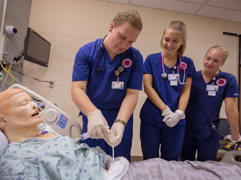 Third-year nursing student Andrew Ketchum, left, prepares to aspirate a simulation mannequin’s stomach contents through a gastrostomy tube with classmates Laurel Gurney, center, and Corryl Kemp.