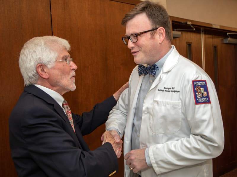 Dr. Lincoln Arceneaux, left, is congratulated by Dr. Brad Ingram, assistant professor of pediatric neurology, who paid tribute to his former professor during the room-naming ceremony Thursday.