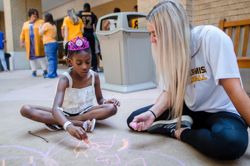 Southern Miss volleyball player Madison Lawler draws a sidewalk chalk mural with patient Zylee Oliver of Fayette.