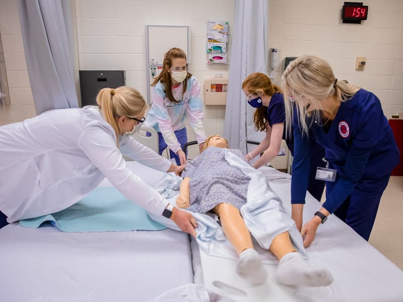 School of Nursing instructor Hannah Hogg, second from left, coaches Accelerated BSN students in moving a "patient" from stretcher to bed in a nursing simulation lab.