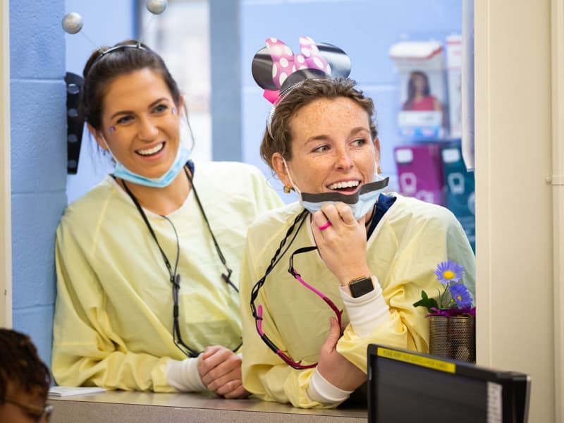Two dental hygiene students lean out of interior office window.