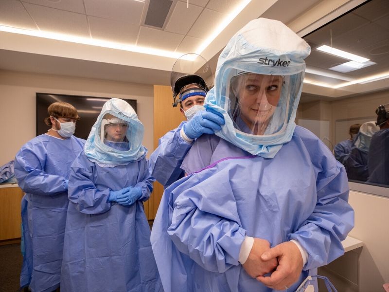 John Carter, left, MICU nurse, helps Jessie Harvey, second from left, assistant professor of medicine, pulmonary, don protective gear while J. D. Chisolm, second from right, MICU nurse, does the same for Kelly Jones, respiratory therapy supervisor, during a pilot training session in the Simulation Center.