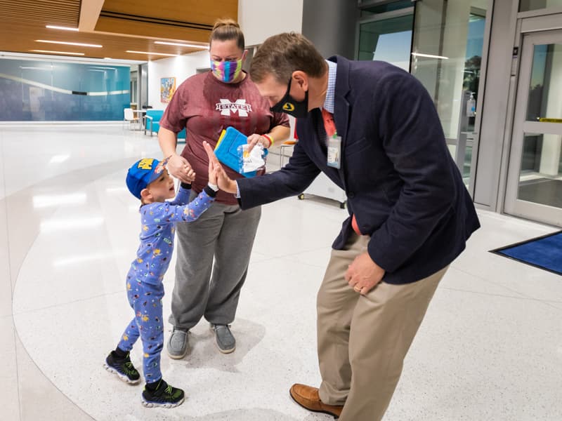 After hand-sanitizing, Dr. Guy Giesecke, Children's of Mississippi CEO, and Jovi McCloud of Morton, the first patient to enter the Kathy and Joe Sanderson Tower at Children's of Mississippi, share a high-five as Jovi's mother, Amy McCloud, watches with approval.