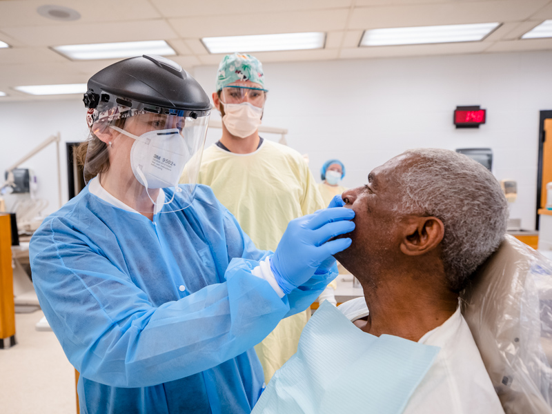 Dr. Tracy Dellinger checks how the bite of Wilbert McGee's new dentures lines up as fourth-year SOD student Trent Johnson observes.