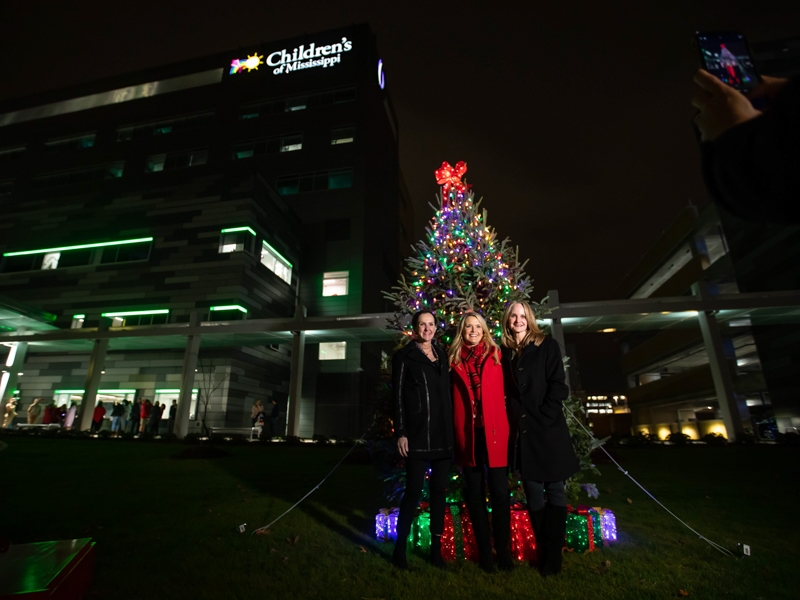 From left, Katy Sanderson Creath, Friends of Children's Hospital Executive Director Rochelle Hicks, and Emily Sanderson Whitaker smile for a photo by the Christmas tree in front of the Kathy and Joe Sanderson Tower at Children's of Mississippi.
