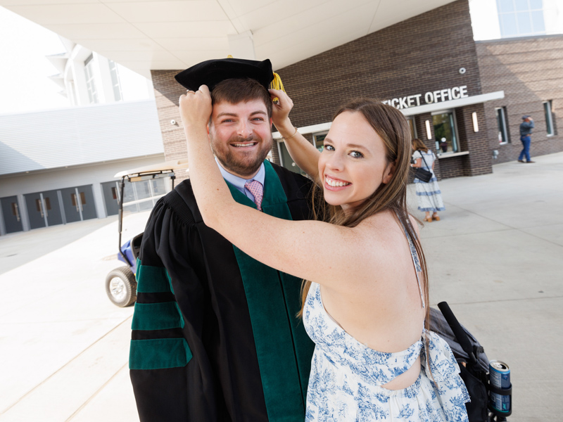 School of Medicine graduate Jacob Simmons gets some wardrobe assistance from his wife, Kaitlyn Simmons, before commencement exercises. Joe Ellis/ UMMC Communications 