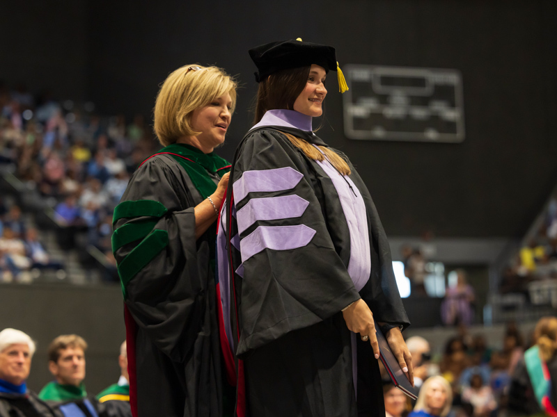 Dr. LouAnn Woodward places a hood over the shoulders of her daughter, Julianna Woodward Steinle, who received the Doctor of Dental Medicine during commencement. Melanie Thortis/ UMMC Communications 