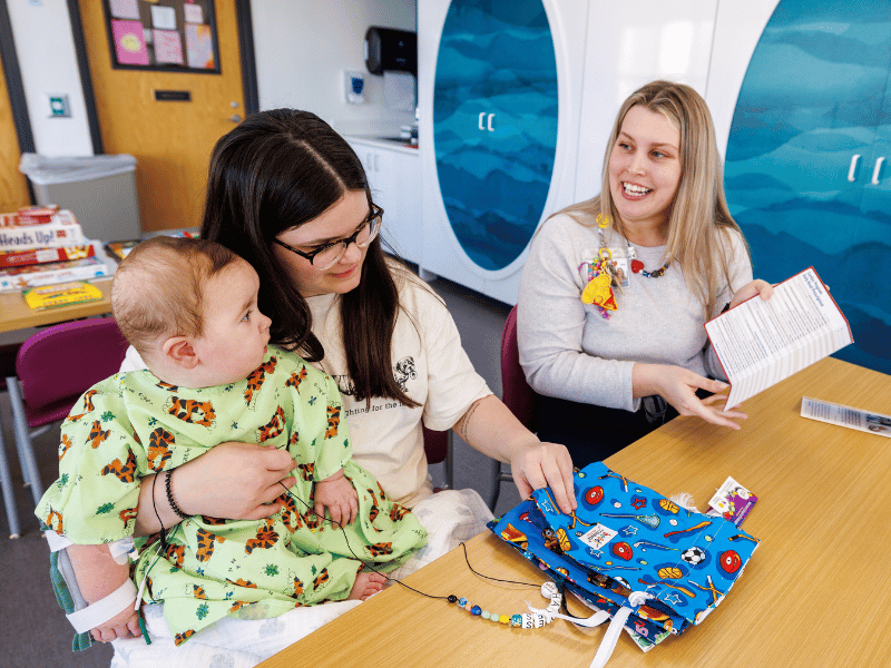 Children's of Mississippi child life specialist Allyson Holliman, right, tells Riley Strickland and son Hayes Clayton about the Beads of Courage program.