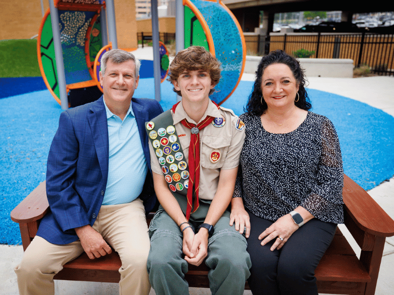 Felton Walker smiles beside his parents, Chip and Liz Walker, as the three share one of the benches he built and donated to Children's of Mississippi.