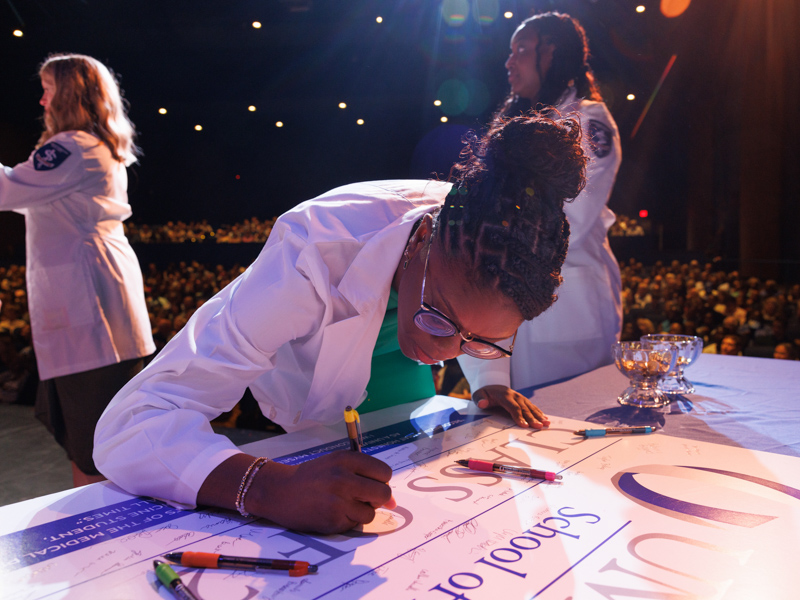 Danielle Holliday writes her name alongside those of her fellow medical students in the Class of 2028.