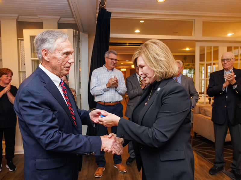 Dr. John Hall receives a 50-year pin from Dr. LouAnn Woodward, vice chancellor for health affairs and dean of the School of Medicine. Among those applauding is Dr. James Keeton, right, vice chancellor from 2009 to 2015. Jay Ferchaud/ UMMC Communications 