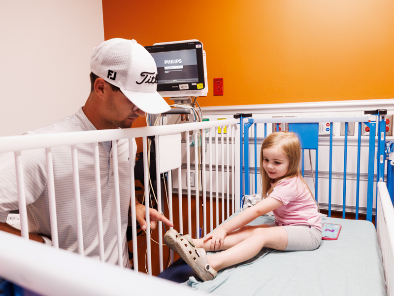 Chesleigh Miller, big sister to imaging patient Charlie Miller of Meridian, shows professional golfer Philip Knowles the decorations on her Crocs.