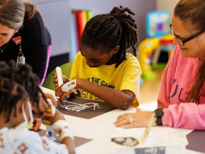 Children's of Mississippi patients Kameron Snow, center, of Byram and Termondtrez Simmons of Yazoo City create images of the bones of their hands with hospital school teachers Allyn Anderson, left and Lori Henry.