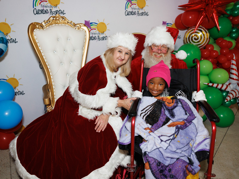 Children's of Mississippi patient Amaya Fields of Summit smiles with Santa and Mrs. Claus during BankPlus Presents Light-A-Light. Jay Ferchaud/ UMMC Communications 