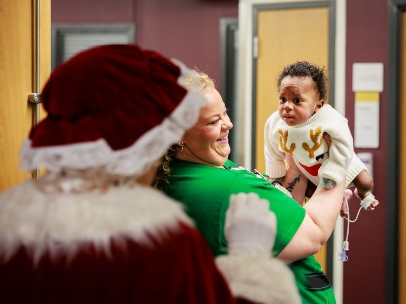 NICU shift supervisor Carly Tuura holds patient Zy'Aire Magee of Byram as Mrs. Claus looks on.