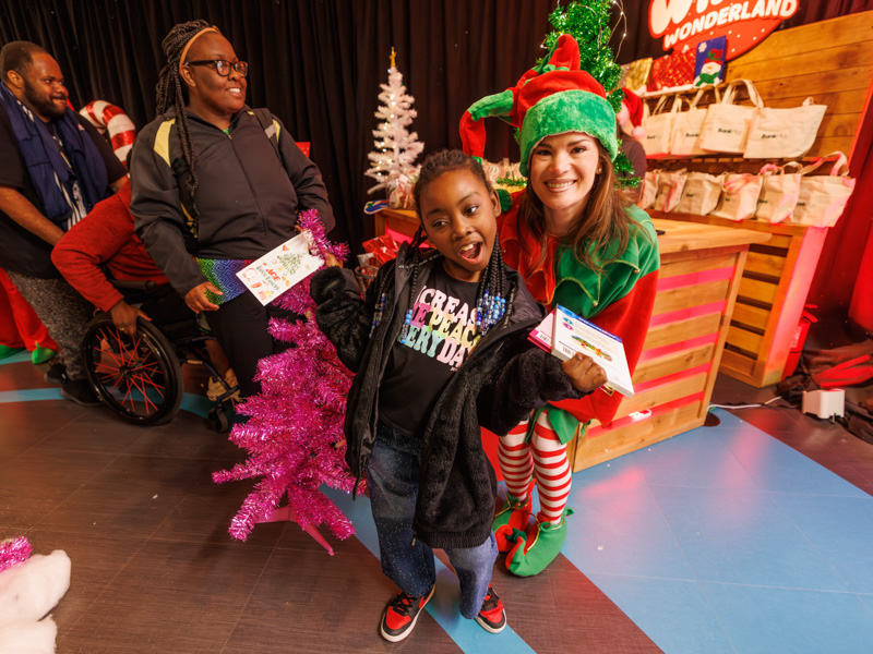 Arielle Mitchell of Pascagoula smiles with a volunteer elf during BankPlus Presents Winter Wonderland and Ace Tree Farm. Melanie Thortis/ UMMC Communications 