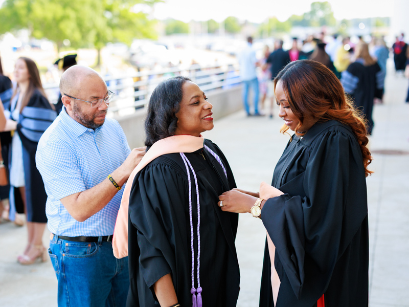 Masters of Science in Nursing graduates Loretta Brown, center, and Darcy Newton get ready for commencement with help from Brown's fiancé Eric Bluntson. Joe Ellis/ UMMC Communications