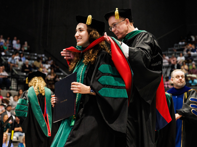 Caroline Doherty is hooded by her father, Dr. Michael Doherty, professor in radiology. Jay Ferchaud/ UMMC Communications