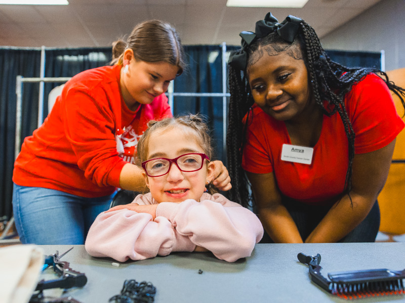Students Gabriella and Amya put the finishing touches on Emma Porch's braids.