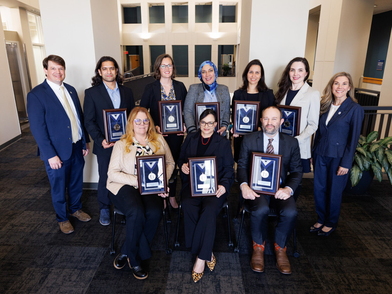 Dr. Lee Bidwell, left, associate vice chancellor for research, and Dr. Caroline Compretta, right, assistant vice chancellor for research, congratulate silver medallion winners, seated from left, Dr. Candace Howard-Claudio, professor of radiology; Dr. Amy Kohtz, assistant professor of psychiatry; Dr. Matthew Kutcher, associate professor of trauma and critical care surgery; and standing, Dr. Utsav Nandi, associate professor of emergency medicine; Dr. Hanna Broome, associate professor of cell and molecular biology; Dr. Noha Elsayed, assistant professor of pharmacology and toxicology; Dr. Lorena M. Amaral, associate professor of pharmacology and toxicology; and Dr. Brigitte Martin, assistant professor of cell and molecular biology.