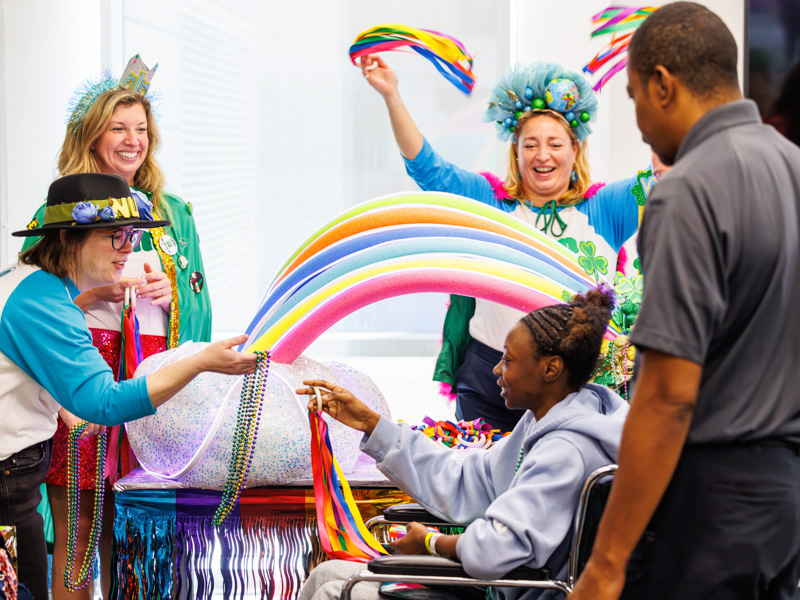 Kalia Evans, 17, of Learned, partakes in the St. Patty's themed cheer with her dad Jonathan Evans as members of the Nugget League of Mayhem krewe, from left, Sophie McNeil Wolf, Miriam Bond and Jane Jones celebrate during the 2026 Petite Parade at the children's hospital. Melanie Thortis/ UMMC Communications