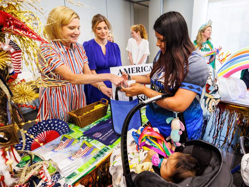 Braedon Bell, 6 months, of Conehatta and his mom Shenita Bell receive an America 250 coloring book from First Lady Elee Reeves and Shelby Wilcher at the 2026 Petite Parade at the children's hospital. Melanie Thortis/ UMMC Communications