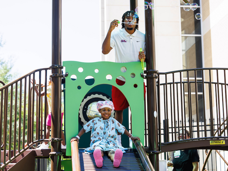 Ole Miss cornerback Jaylon Braxton blows bubbles as Tzuri Elmore, 5, of Greenville slides during a visit from the University of Mississippi football team at Children's of Mississippi.