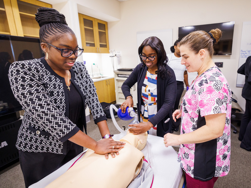 Twins Nyla and Nyja receive hands-on CPR techniques, from Jennifer Harrison at the simulation center, gaining early exposure to clinical skills training through the P.R.O.M.I.S.E. Program at UMMC. Jay Ferchaud/ UMMC Communications