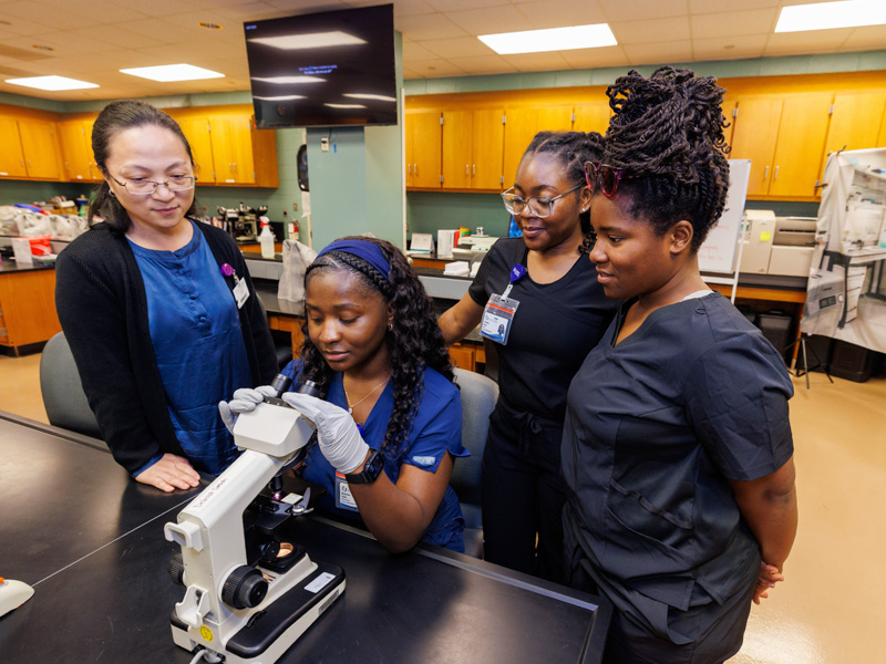 Yin Wang, assistant professor of medical laboratory sciences, left, with new students Mysheaira Taylor, Constance Harper and Jasmine Thompson check out slide samples during orientation week. Jay Ferchaud/ UMMC Communications