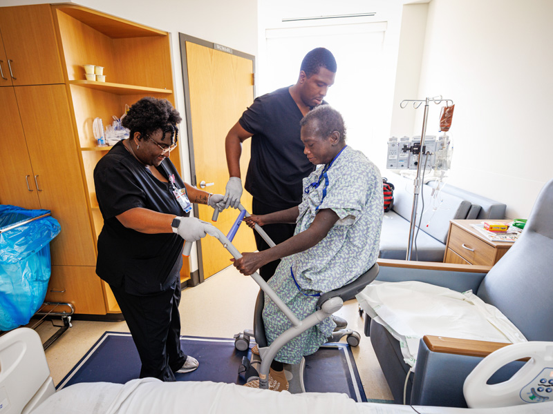 Kayla Kelly, left, and Tavian Johnson, both mobility technicians, work with patient Edna Carson as part of their work to assess mobility during the therapy phase of patient recovery.