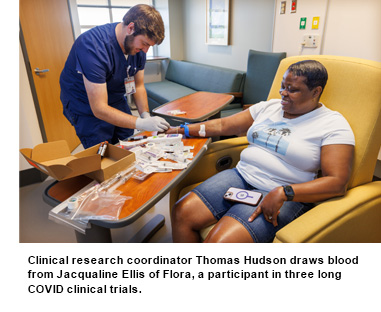 Clinical research coordinator Thomas Hudson draws blood from Jacqualine Ellis of Flora, a participant in three long COVID clinical trials.